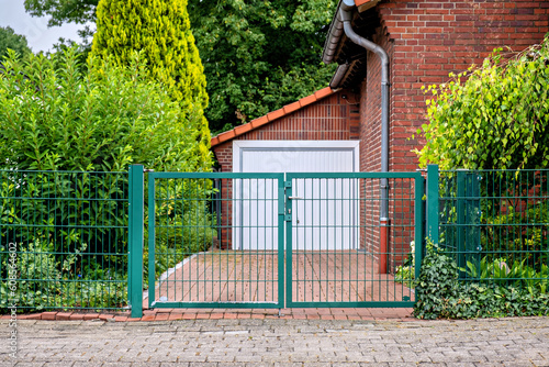 Brick garage with white door and green gate attached to a building in Germany.