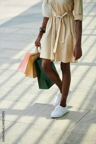 Cropped image of Black woman in beige denim dress and white trainers