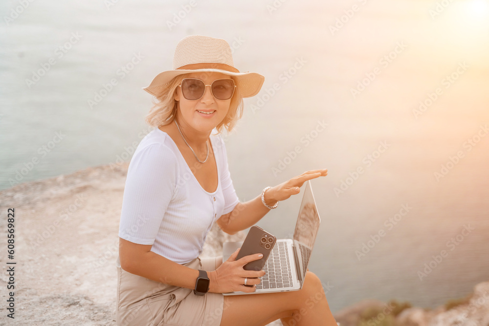 Freelance women sea working on the computer. Good looking middle aged woman typing on a laptop keyboard outdoors with a beautiful sea view. The concept of remote work.