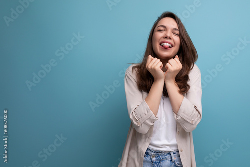 joyful happy young dark-haired lady in informal clothes celebrating victory on blue background