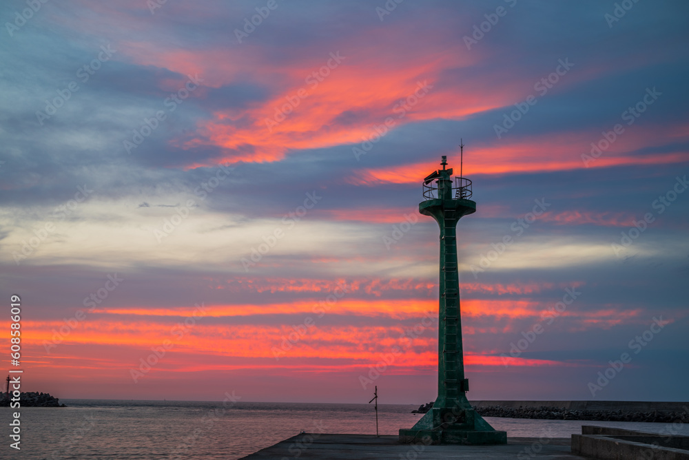 The lighthouse at harbor with burning sky in golden hour. The quite beautiful orange tone sunset at Tainan quigu of Taiwan. The sky had fantastic hue and the sea had the wonderful reflection of light.