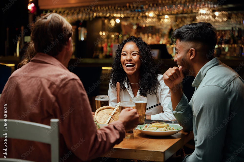 Happy young multiracial group of friends in casual clothing laughing around table with food and drinks