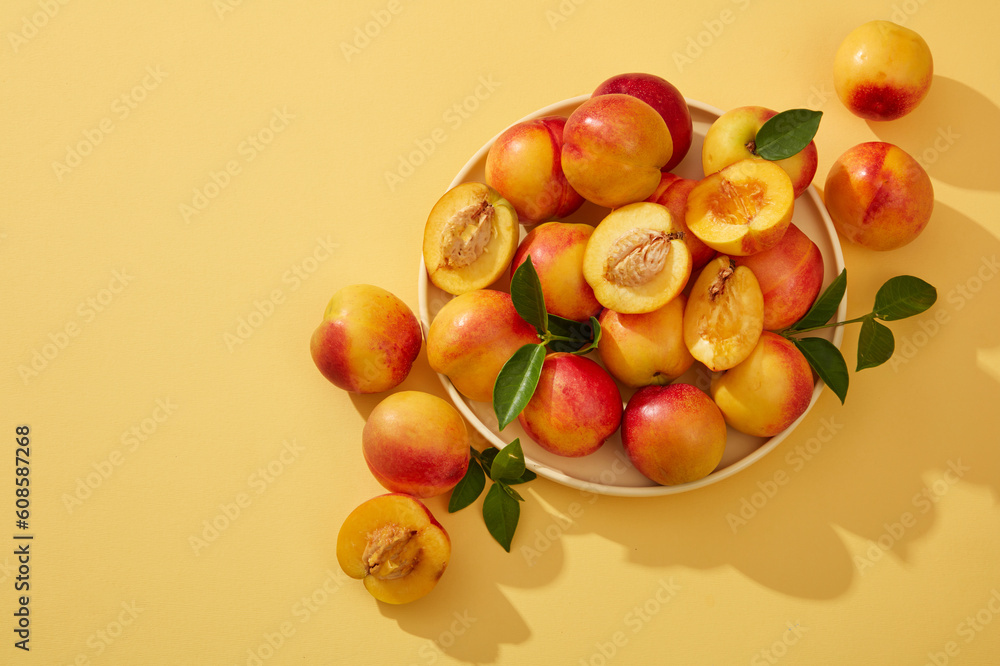 Colorful fresh ripe peaches (prunus persica) with green leaves on the stem are placed on a round plate and decorated on a yellow background. Minimal scene with copy space Colorful fresh ripe peaches (prunus persica) with green leaves on the stem are placed on a round plate and decorated on a yellow background. Minimal scene with copy space