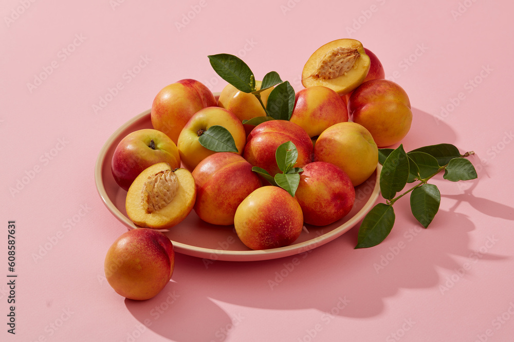 Against the pastel pink background, a dish of some peaches is displayed. Peach (Prunus persica) helps enhance health condition with vitamin A and C Against the pastel pink background, a dish of some peaches is displayed. Peach (Prunus persica) helps enhance health condition with vitamin A and C