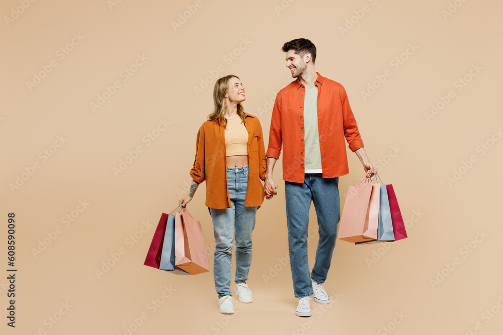 Full body young smiling happy couple two friends family man woman wears casual clothes hold shopping paper package bags together isolated on plain beige background. Black Friday sale buy day concept. Full body young smiling happy couple two friends family man woman wears casual clothes hold shopping paper package bags together isolated on plain beige background. Black Friday sale buy day concept.