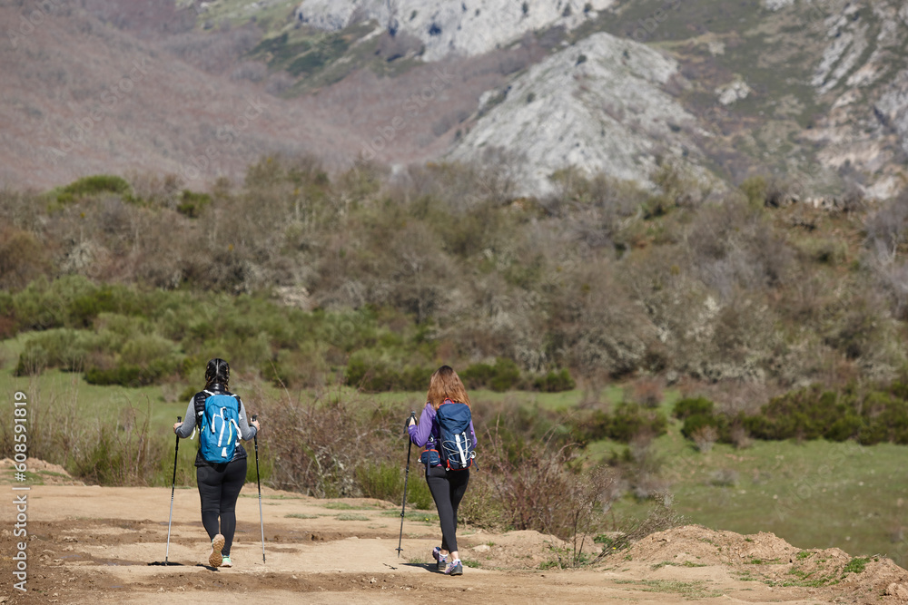 Two female backpacker hikers on a pathway. Mountain trekking. Copyspace