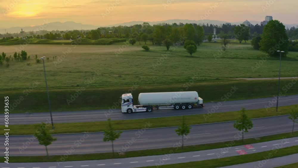 Tanker truck riding on highway in countryside green fields at sunrise aerial view. Lorry trailer shipping cargo and driving on asphalt motorway side view tracking shot Tanker truck riding on highway in countryside green fields at sunrise aerial view. Lorry trailer shipping cargo and driving on asphalt motorway side view tracking shot