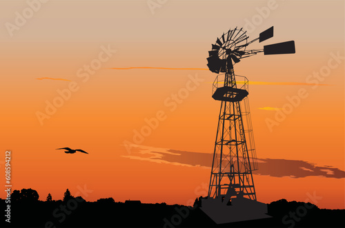Silhouette of a vintage water pumping windmill against sunset sky
