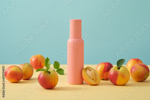 Light blue background with peaches decorated with a beauty cosmetic bottle in pink color. Peach (Prunus persica) extract helps to remove dark circles and blemishes