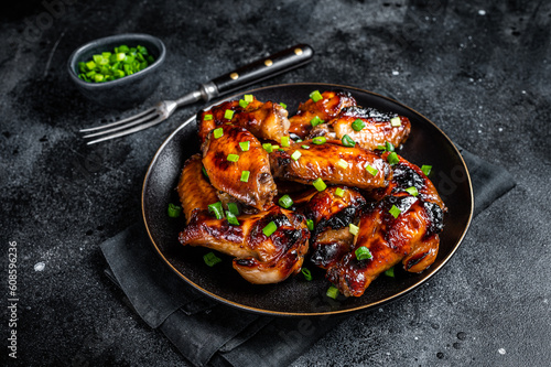 Baked chicken wings with sweet chili sauce in a plate. Black background. Top view