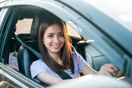 Young beautiful asian women getting new car. she very happy and excited. Smiling female driving vehicle on the road on a bright day.
