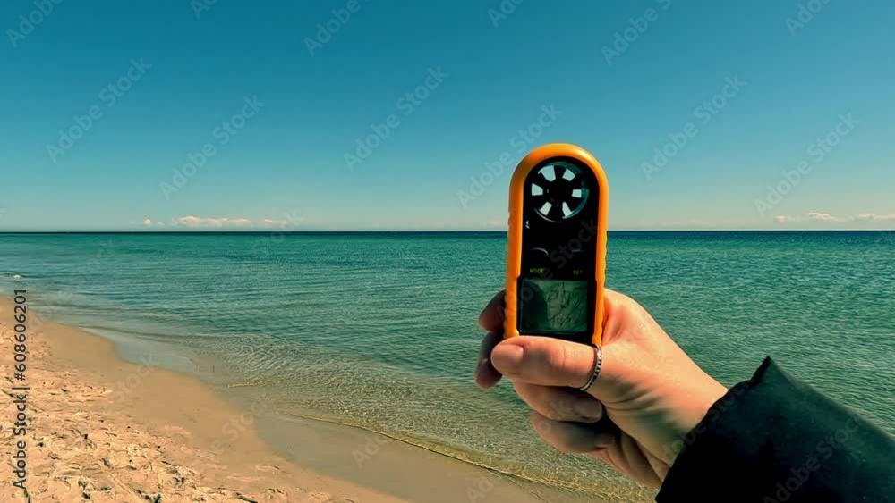 Wind force measurement. Female hand holding a device for measuring wind strength on the sea beach. Anemometer.