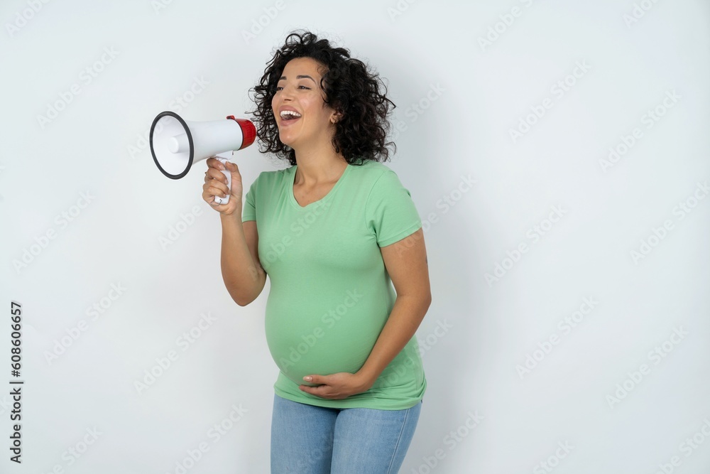 Funny Beautiful pregnant woman wearing green T-shirt standing over white studio background People sincere emotions lifestyle concept. Mock up copy space. Screaming in megaphone. Funny Beautiful pregnant woman wearing green T-shirt standing over white studio background People sincere emotions lifestyle concept. Mock up copy space. Screaming in megaphone.