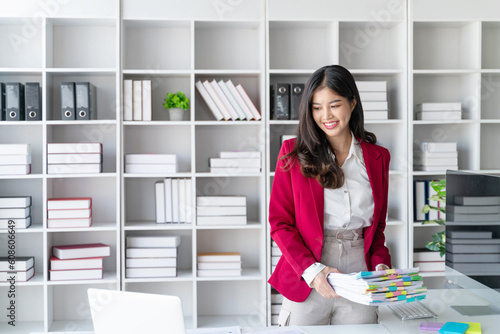 Asian happy beautiful businesswoman hold paper documents work stand at workplace. Attractive female employee office worker smile.
