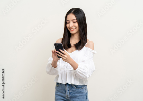 Pretty young asian woman using smartphone standing on isolated white background. Excited Beautiful young asian shopping online payment with mobile phone. Playing game on smartphone