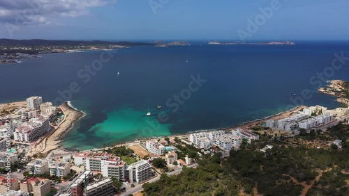 Aerial drone footage of the town of Sant Antoni de Portmany on the west coast of Ibiza Spain’s Balearic Islands, showing the drone landing in the wooded area by the ocean front in the summer time photo