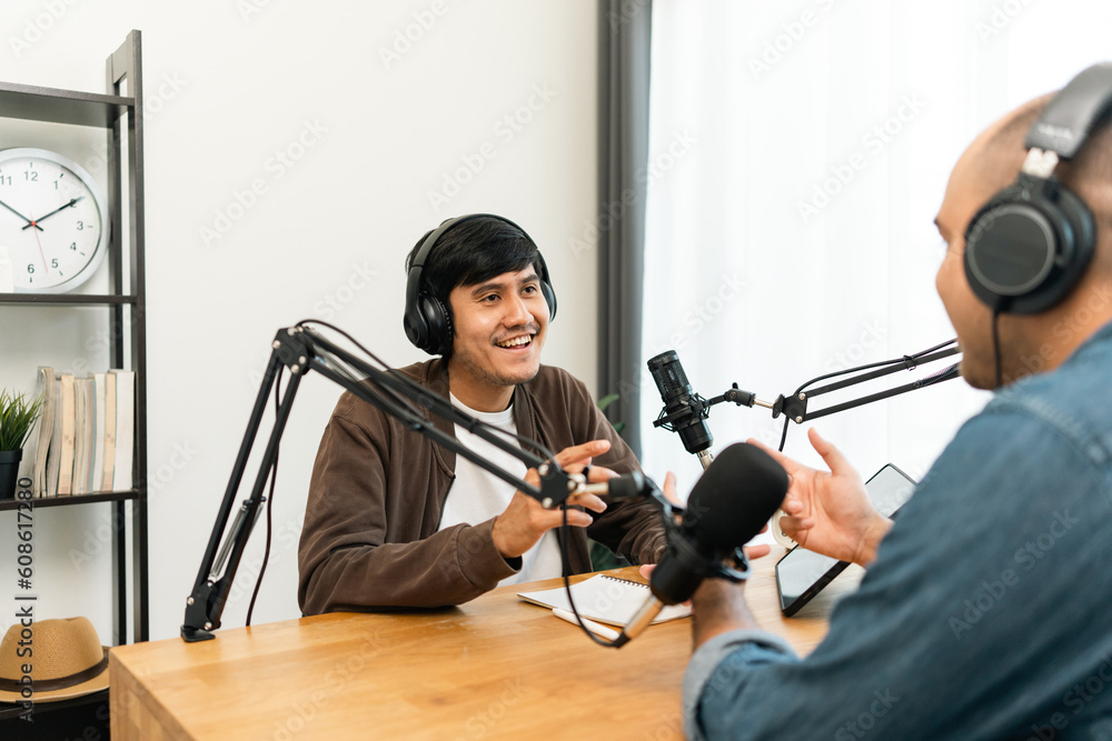 Young asian man host streaming podcast with condenser microphone work on tablet at small broadcast home studio. Content creator blogger recording voice over radio interview guest conversation