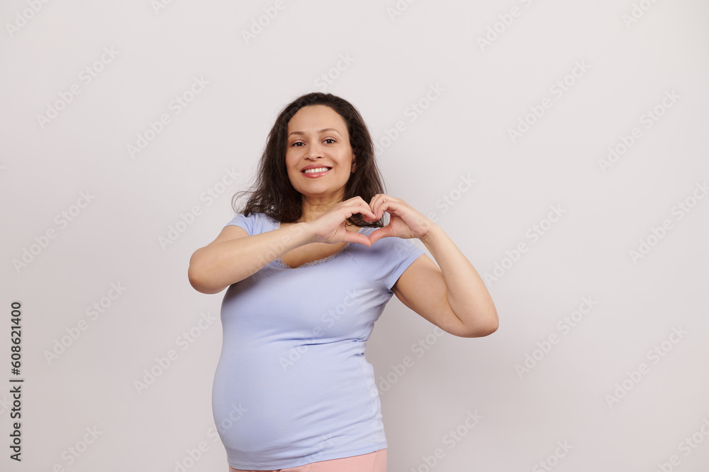 Beautiful pregnant woman smiling at camera, forming a heart shape with ...