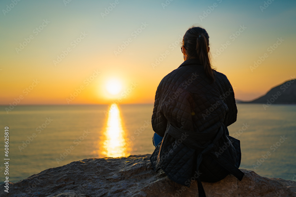 Woman enjoy of brightly colored sunset over the calm Mediterranean Sea, rear shot