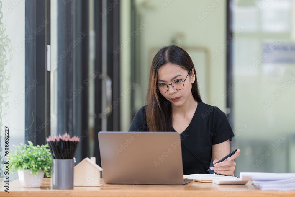 A beautiful young Asian businesswoman is saving and checking work and documents with her laptop computer at her desk with a bright smile on her face. A beautiful young Asian businesswoman is saving and checking work and documents with her laptop computer at her desk with a bright smile on her face.