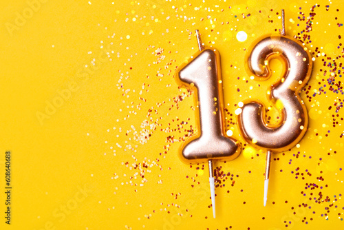 Gold candles in the form of number thirteen on yellow background with confetti. 13 years celebration.