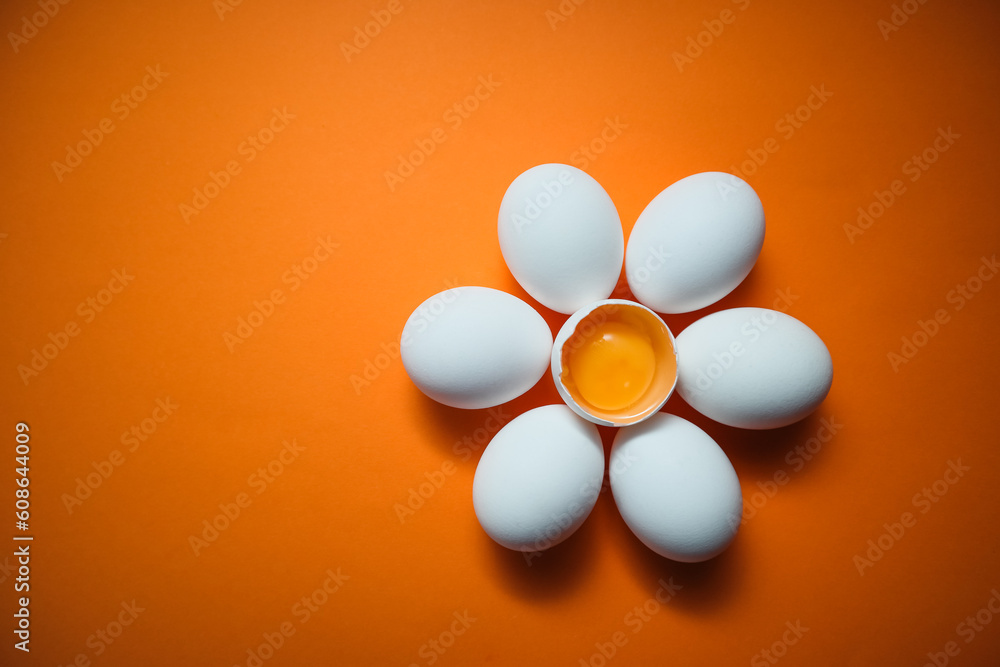 Flower shaped raw egg on orange background. Few white eggs, whole and broken egg half with a yolk isolated on a white background Flower shaped raw egg on orange background. Few white eggs, whole and broken egg half with a yolk isolated on a white background