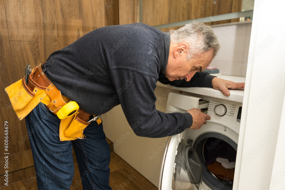 an elderly man repairs a washing machine an elderly man repairs a washing machine