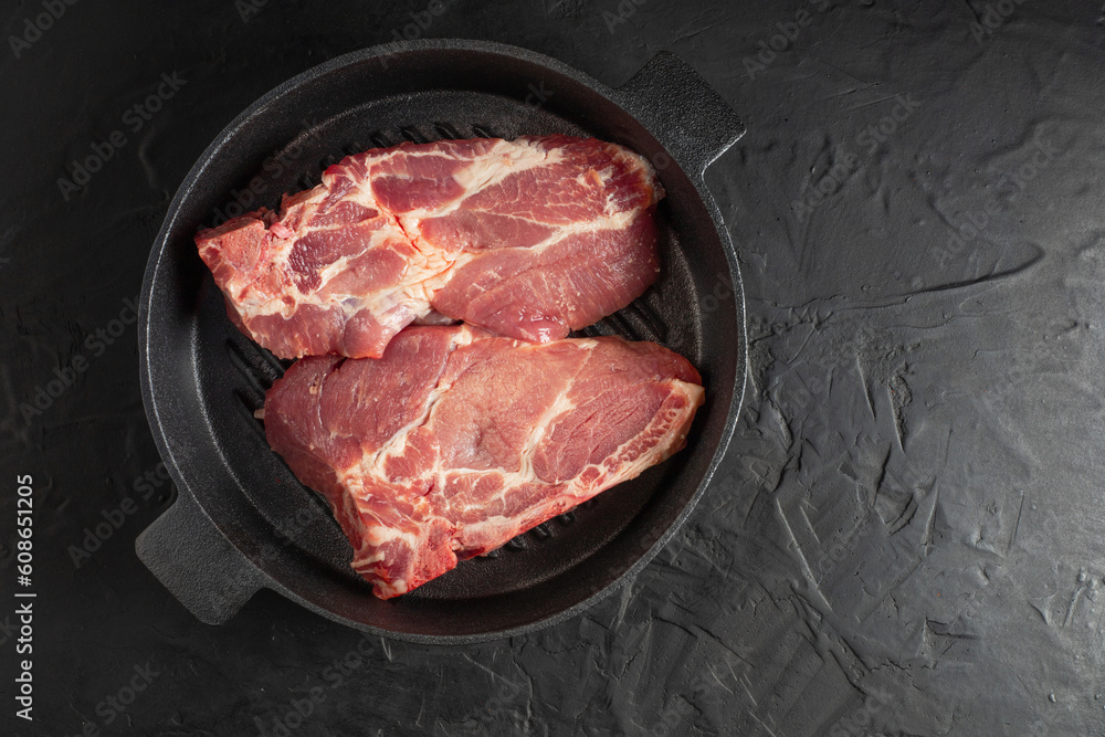 fresh deli meat steaks on a black skillet on a black background with free space for text