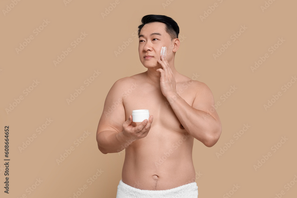 Fototapeta premium Handsome man applying cream onto his face on light brown background