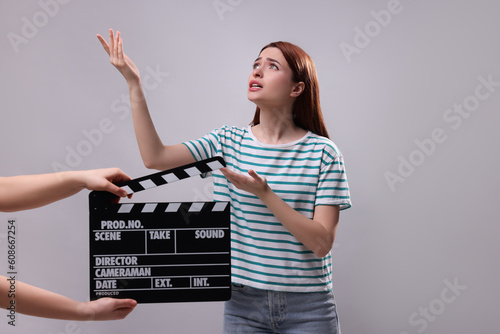 Emotional actress performing role while second assistant camera holding clapperboard on grey background