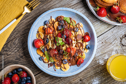 Small American pancakes mixed with seasonal fruit like strawberries, blueberries and cherries. Dipped with melted chocolate, placed on a rustic wooden board. 