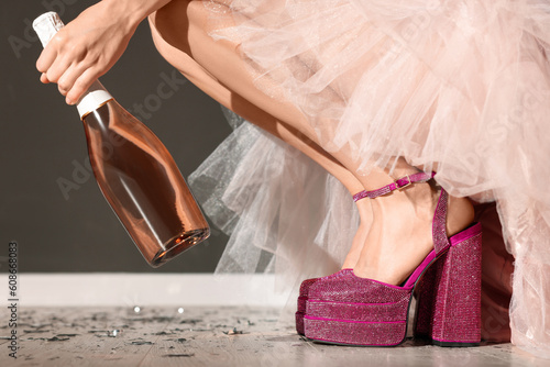 Stylish party. Woman wearing pink high heeled shoes with platform and square toes holding bottle of wine indoors, closeup photo