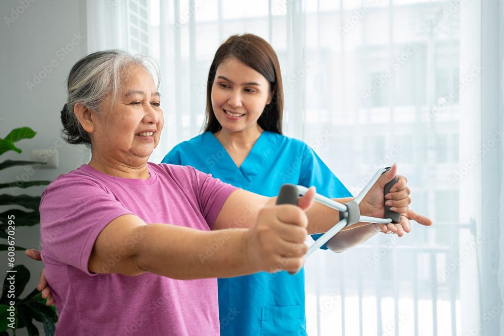Happy elderly female exercising with rubber expander with Young physiotherapist for recovery arm muscles in a physiotherapy center. Concept of happy retirement with care from a caregiver and health. Happy elderly female exercising with rubber expander with Young physiotherapist for recovery arm muscles in a physiotherapy center. Concept of happy retirement with care from a caregiver and health.