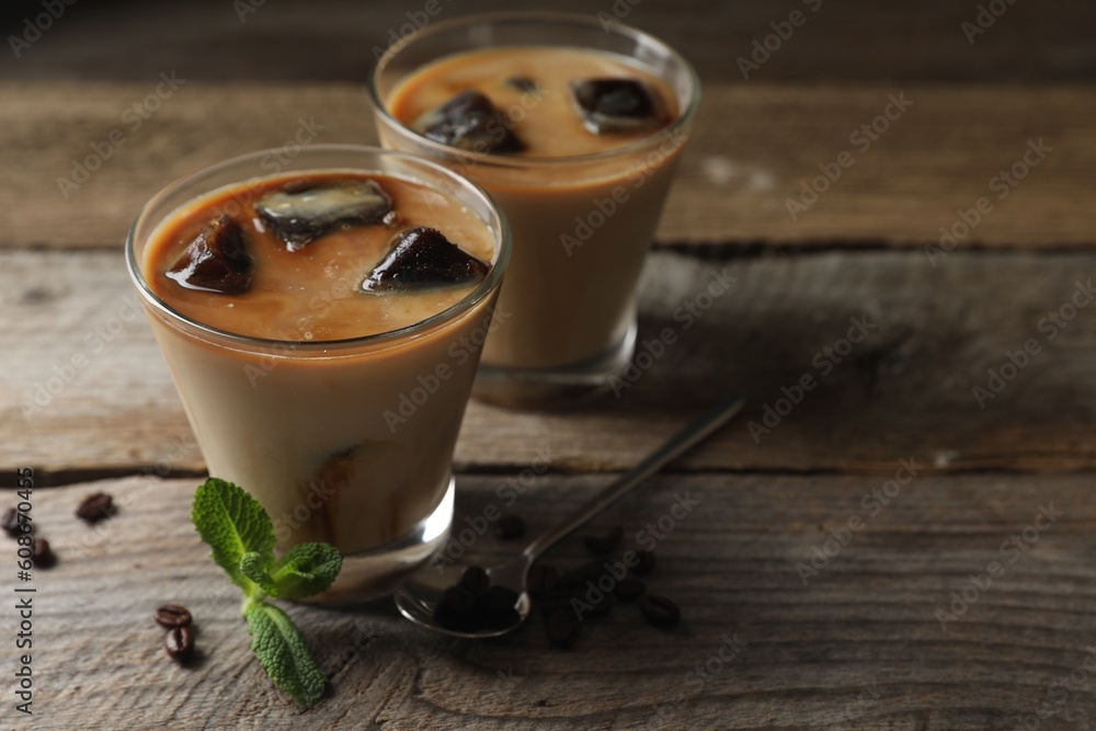 Glasses of delicious iced coffee with milk, beans and mint on wooden table, space for text Glasses of delicious iced coffee with milk, beans and mint on wooden table, space for text