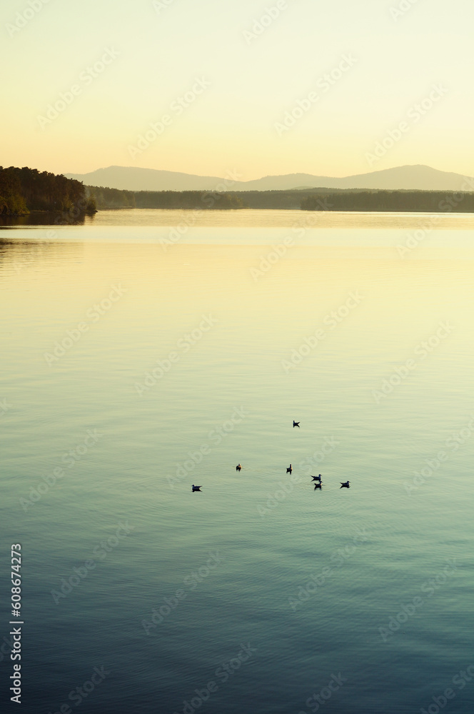 Fototapeta premium Summer water landscape, sunset lake and the mountains at the horizon lit by evening sunlight