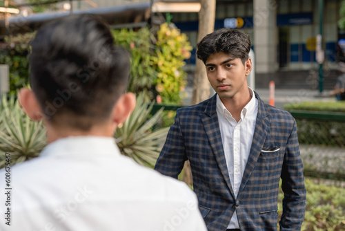 A hotheaded young indian man stares down his workmate while outside the office. Animosity in the workplace.