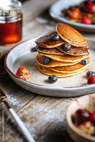 American pancakes with blueberries, strawberries and cherries with dip of honey. Placed on a rustic designer plate, on wooden rustic board. 