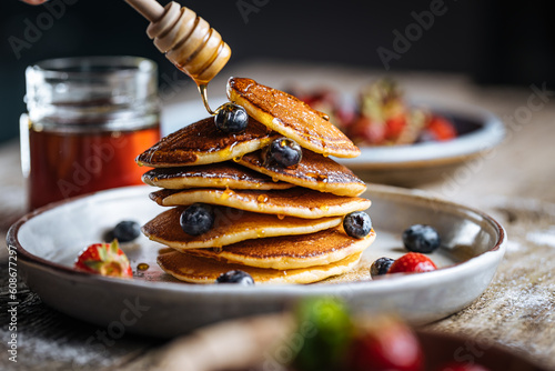 American pancakes with blueberries, strawberries and cherries with dip of honey. Placed on a rustic designer plate, on wooden rustic board. 