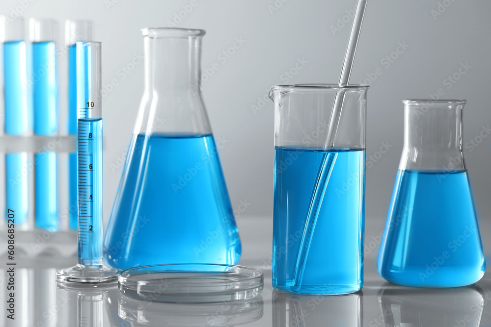 Different laboratory glassware and test tubes with light blue liquid on table