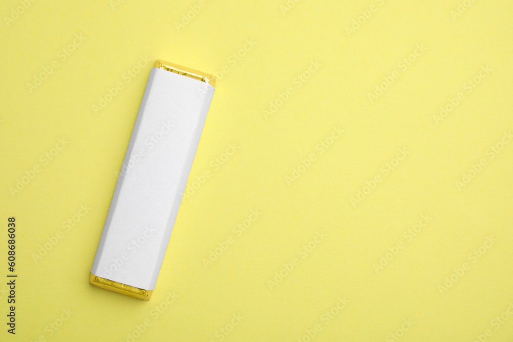 Tasty chocolate bar in package on light yellow background, top view. Space for text Tasty chocolate bar in package on light yellow background, top view. Space for text