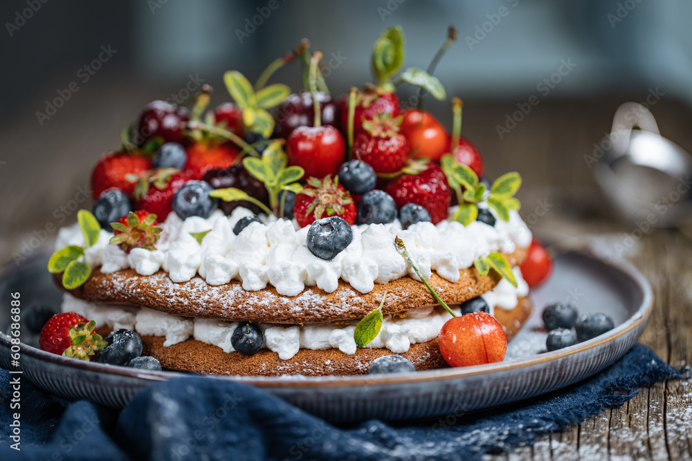 Fresh seasonal layered cake with spring ripe fruit like strawberries, blueberries and cherries. Placed on a elegant blue plate on rustic wooden board Fresh seasonal layered cake with spring ripe fruit like strawberries, blueberries and cherries. Placed on a elegant blue plate on rustic wooden board