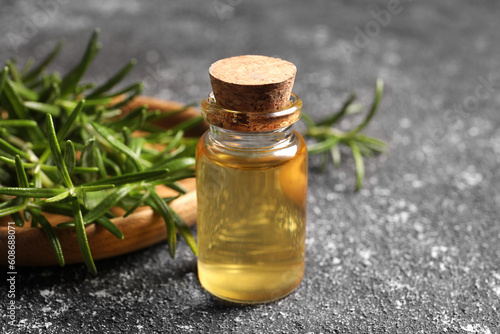 Bottle with oil and fresh rosemary on grey textured table, closeup