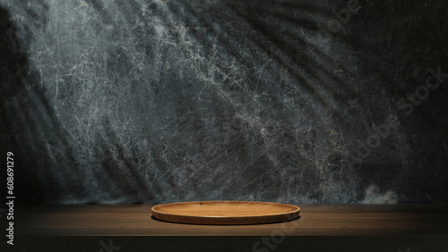 Round wooden plate on the table with dark marble wall background. Light shadow on the wall.