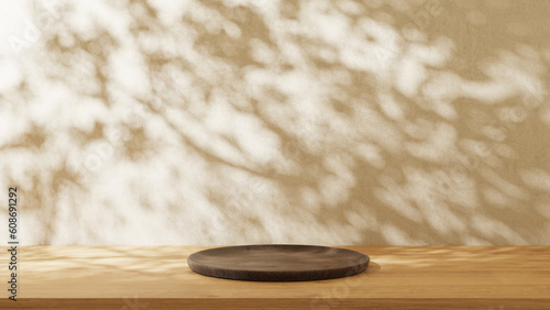 Round wooden plate on the wooden table with light wall background. Leaves shadow on the wall.