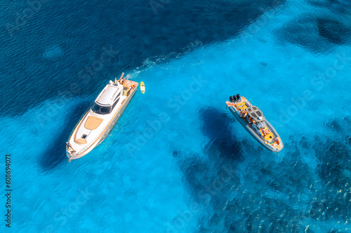 Aerial view of luxury yacht and motorboat on blue sea at sunset in summer. Travel and vacation in Sardinia, Italy. Drone view from above of speed boats, ocean, transparent turquoise water. Seascape © den-belitsky