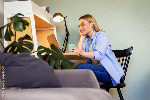 Smiling woman working remotely using laptop from the comfort of her home. photo