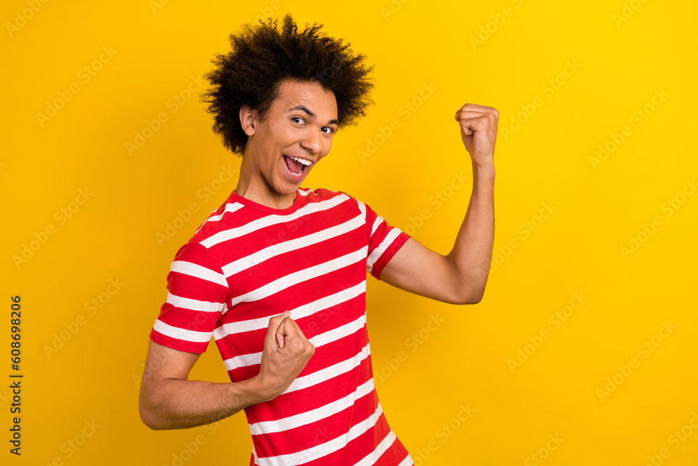 Portrait with young overjoyed guy raise fists express delight glad wear striped shirt white pants isolated yellow color background Portrait with young overjoyed guy raise fists express delight glad wear striped shirt white pants isolated yellow color background