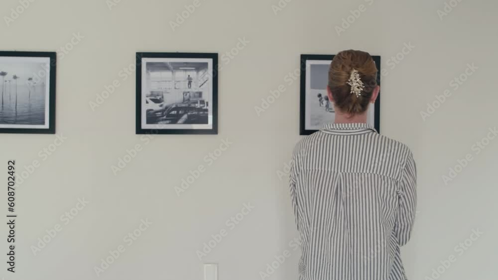 Young female visitor walking in gallery and looking at black and white photos on walls on art exhibition Young female visitor walking in gallery and looking at black and white photos on walls on art exhibition