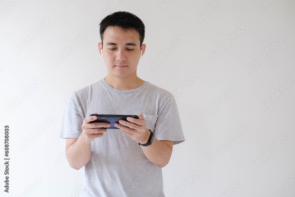 A young Asian man wearing a gray t-shirt is playing game on the smartphone. Isolated white background. A young Asian man wearing a gray t-shirt is playing game on the smartphone. Isolated white background.