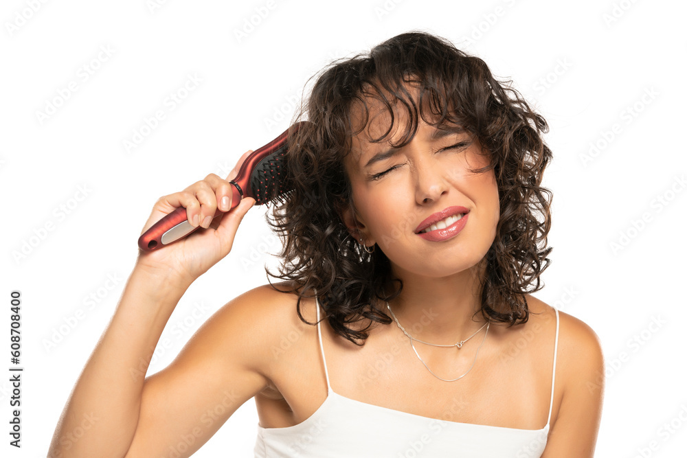 Fototapeta premium Young dark skinned woman with makeup has a problem with combing her wavy hair on a white background